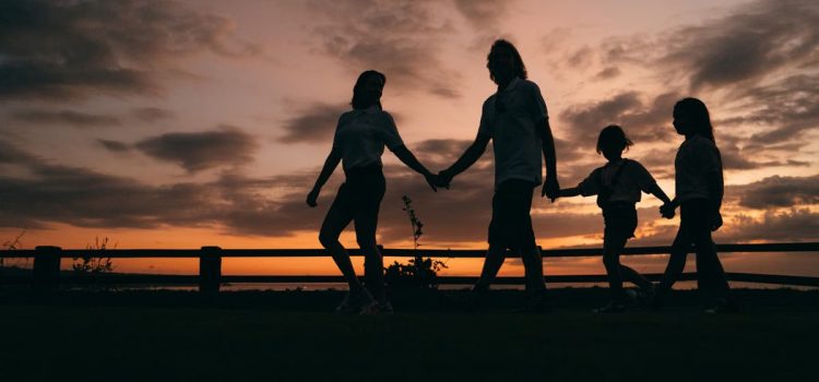 Attività da fare in famiglia per un benessere condiviso A family walks hand in hand against a vibrant sunset, evoking togetherness and peace.